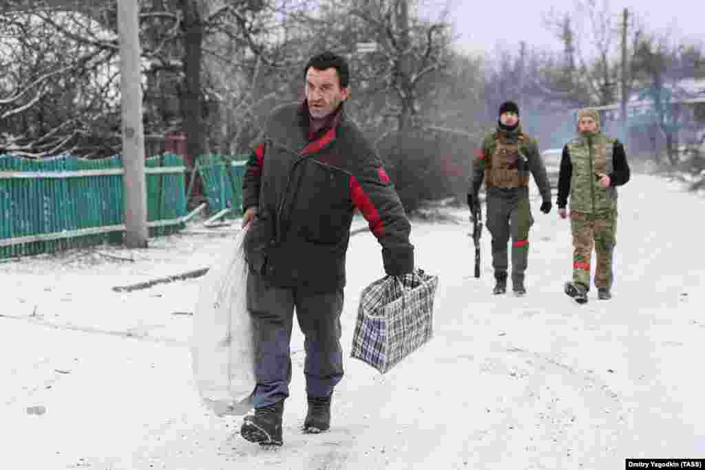 Житель идёт по улице на окраине Авдеевки, за ним — российские военные. 19 февраля 2024 года. Когда в феврале российские войска приблизились к Авдеевке, остававшиеся в городе жители бежали. Неясно, сколько человек решили остаться 