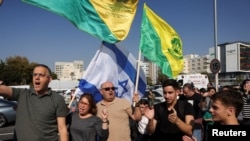 Oamenii țin steagurile Organizației Golani Nonprofit și un steag israelian în ziua eliberării ostaticei israeliene, Agam Berger, soldat capturat de la baza sa militară în timpul atacului din 7 octombrie 2023.