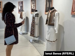 O femeie din Iași admiră câteva dintre costumele tradiționale din colecția Marius Matei. Iunie 2025.
